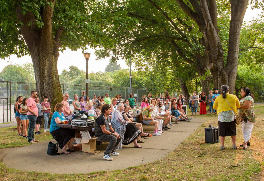 A large group of people at a park listening to one person speak