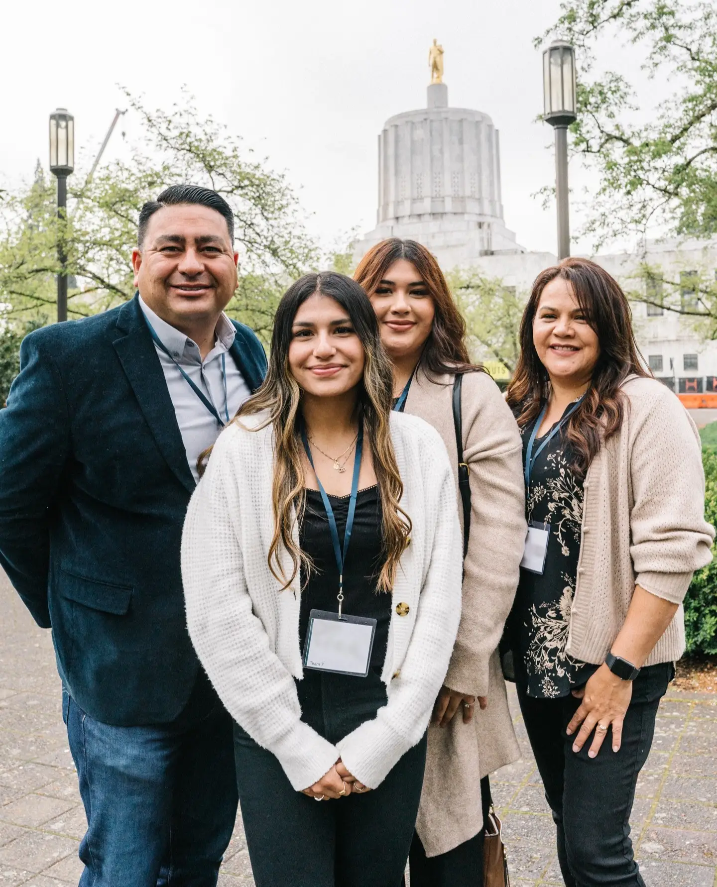 A portrait photo of four people standing with the Oregon Capital in the background